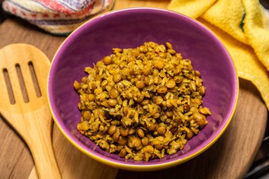 A crockery bowl with brown rice and lentils on a wooden surface, with a wooden spoon and a yellow cloth in the background.