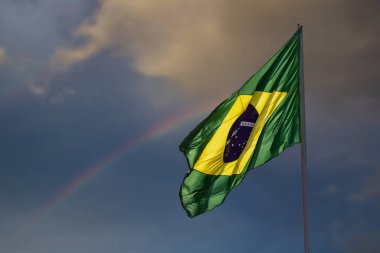  The flag of Brazil. Brazil flag flying, fluttering in the wind and with the sky and rainbow in the background.