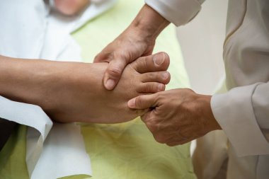 A professional doing therapeutic massage on the foot of the patient who is lying on the stretcher.