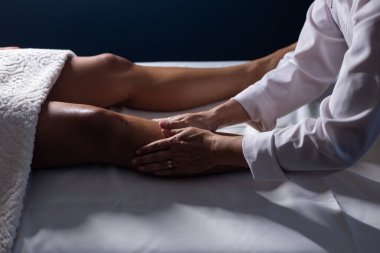 A professional giving therapeutic massage to the legs of a patient who is lying on a stretcher.