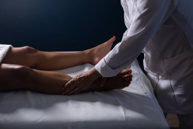 A professional giving therapeutic massage to the legs of a patient who is lying on a stretcher.