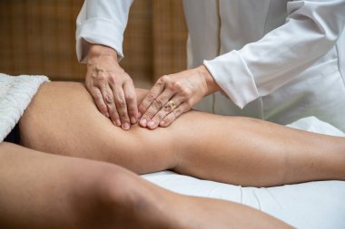 A professional doing therapeutic massage on the knee of the patient who is lying on the stretcher.
