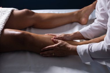 A professional doing therapeutic massage on the leg of the patient who is lying on the stretcher.