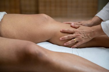 A professional doing therapeutic massage on the leg of the patient who is lying on the stretcher.