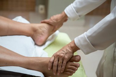 A professional doing therapeutic massage on the feet of the patient who is lying on the stretcher.