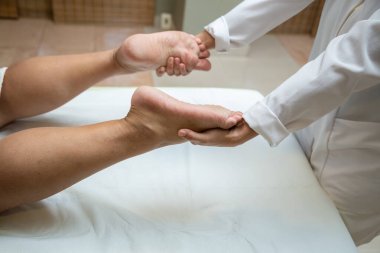A professional doing therapeutic massage on the feet of the patient who is lying on the stretcher.