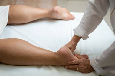 A professional doing therapeutic massage on the foot of the patient who is lying on the stretcher.