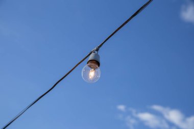 A light bulb connected to an electrical wire with blue sky in the background.