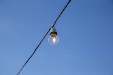 A light bulb connected to an electrical wire with blue sky in the background.