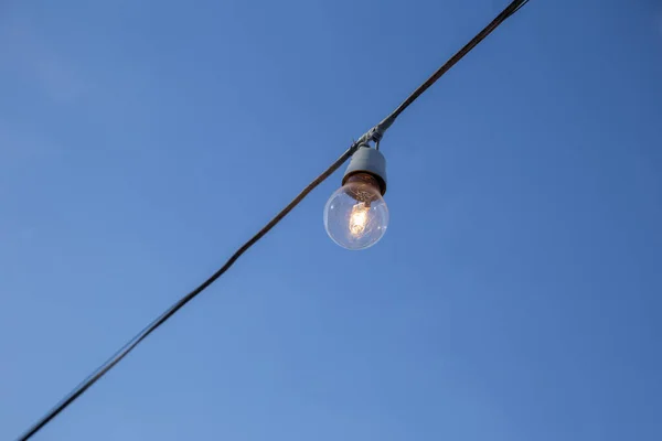 A light bulb connected to an electrical wire with blue sky in the background.