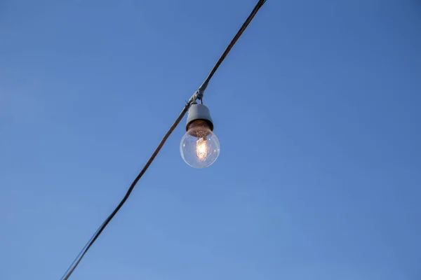 A light bulb connected to an electrical wire with blue sky in the background.