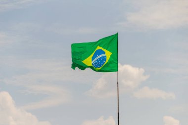 Brezilya bayrağı dalgalanıyor ve rüzgarda dalgalanıyor. Arka planda bulutlu gökyüzü var..