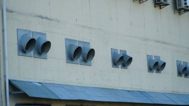 Endüstriyel bir binanın çatısında mavi gökyüzü ve arka planda bulutlar bulunan klima üniteleri (HVAC).