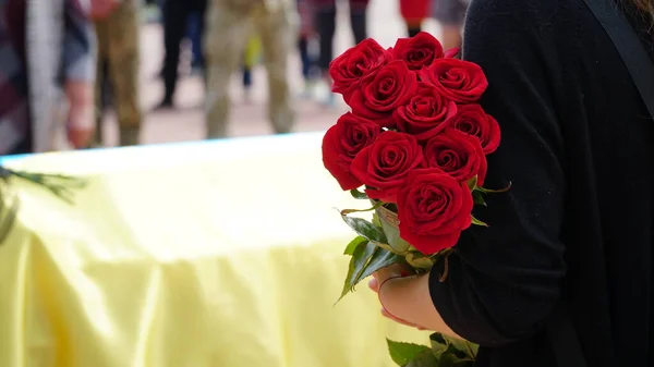 Unhappy woman with red roses and a coffin at a funeral. The funeral ceremony of a soldier. Funeral ceremony. The funeral of Ukrainian soldiers who died during the Russian invasion of Ukraine. n
