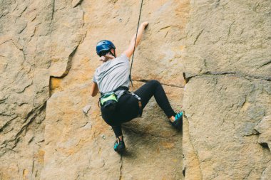 Dışarıdaki kayaların önünde duran ekipmanlı genç adam tırmanmaya hazırlanıyor. Açık hava aktiviteleri için eğitim alanı. Sıra dışı spor.