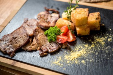 Dilimlenmiş sığır dili, patates ve domatesli siyah taş tahtada.