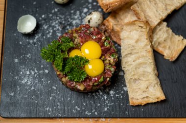 Sığır eti, bıldırcın yumurtası ve ekmekle servis edilir.