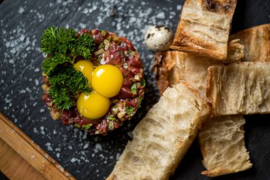 Sığır eti, bıldırcın yumurtası ve ekmekle servis edilir.