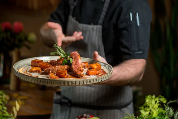 Şef fırında sebzeyle dilimlenmiş sulu biftek gösteriyor.