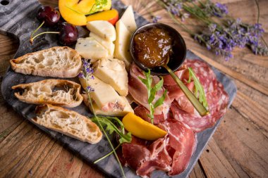 Şık mermer tahtada servis edilen çeşitli et, peynir ve reçelli ekmek.