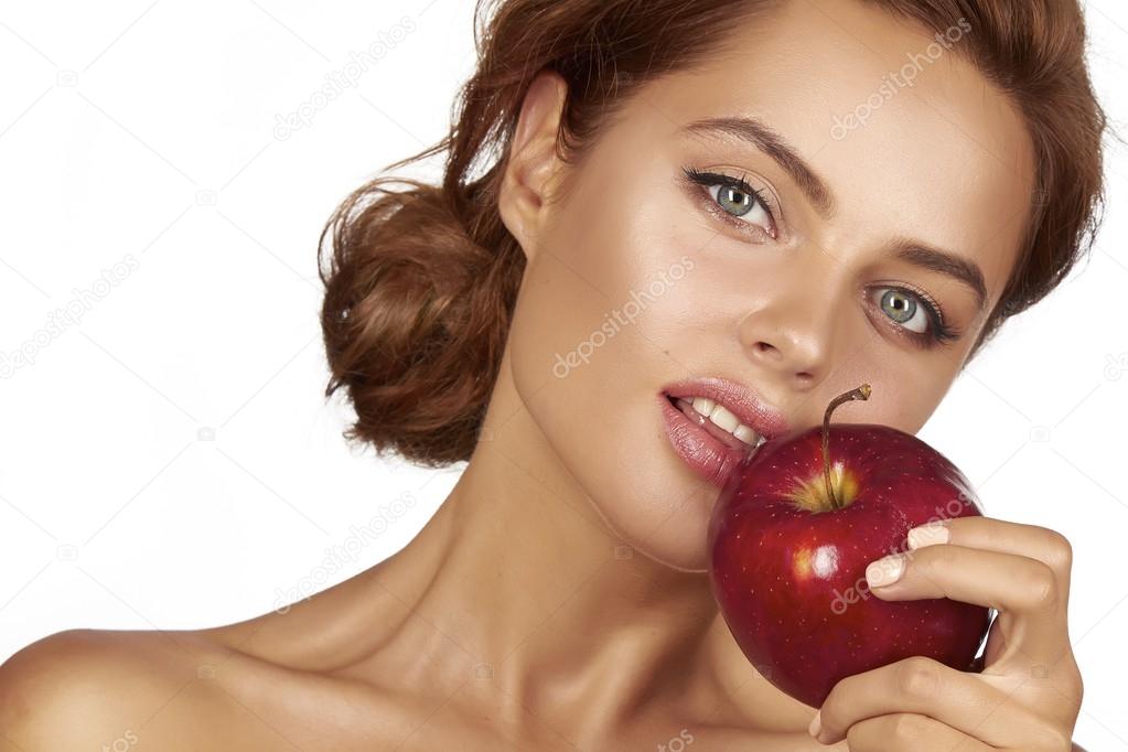 Young beautiful sexy girl with dark curly hair, bare shoulders and neck, holding big red apple to enjoy the taste and are dieting, healthy eating and organic foods, feeling temptation, smile, teeth