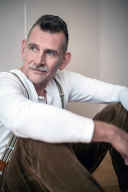 50 'li yaşlarda yerde oturan yakışıklı bir adamın portresi.