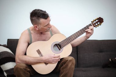 50 'li yaşlarda yakışıklı bir adam kanepede oturup gitar çalıyor.