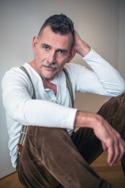 50 'li yaşlarda yerde oturan yakışıklı bir adamın portresi.