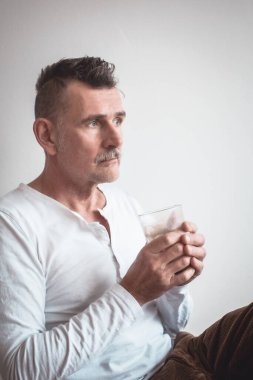 50 'li yaşlarda yakışıklı bir adam oturmuş kahve içiyor.