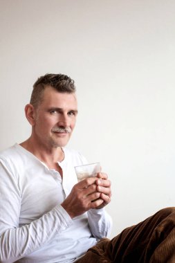 50 'li yaşlarda yakışıklı bir adam oturmuş kahve içiyor.