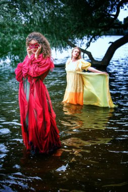 Suda duran tarihi elbiseli iki kadının dramatik portresi.