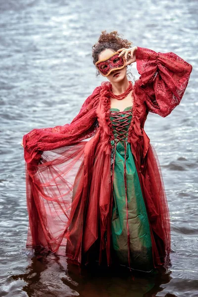赤い歴史的なドレスを着た女性と水の中に立つ仮面舞踏会 — ストック写真