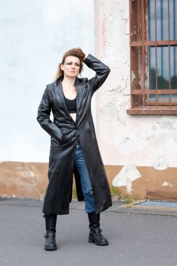 Kot pantolonlu, siyah deri ceketli genç esmer kadın sokakta dikiliyor.