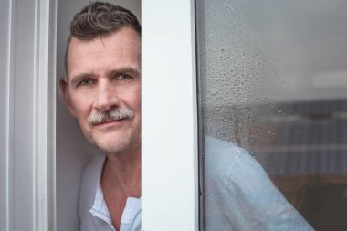 50 'li yaşlarda, pencerenin önünde duran yakışıklı bir adamın portresi.