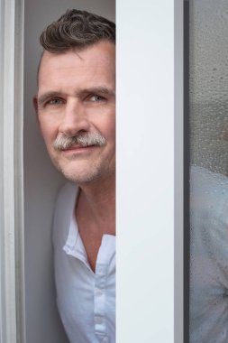 50 'li yaşlarda, pencerenin önünde duran yakışıklı bir adamın portresi.