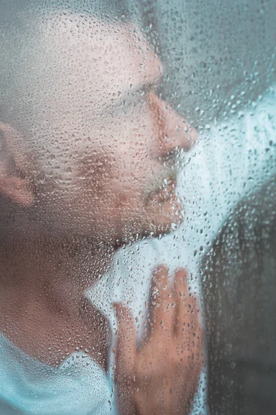 雨の日に窓の外を見る50代のハンサムな男の肖像画 — ストック写真