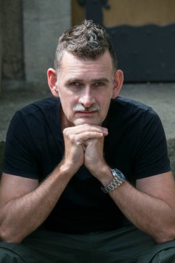 50 'li yaşlarda siyah tişört giyen yakışıklı bir adamın portresi.