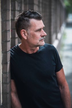 50 'li yaşlarda siyah tişört giyen yakışıklı bir adamın portresi.