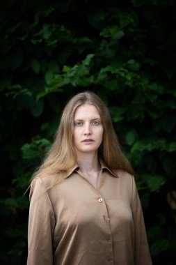 Sarışın genç bir kadının portresi. Açık havada duruyor. Huzurlu görünüyor.