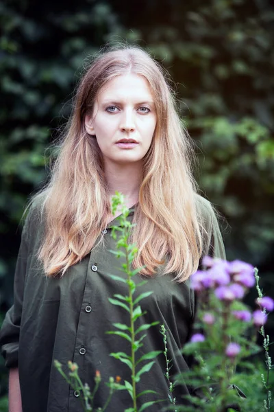 Sarışın genç bir kadının portresi. Açık havada duruyor. Huzurlu görünüyor.