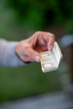 Yaşlı bir kadının eli haplarla dolu bir konteynırı tutarken yakın plan fotoğrafı.