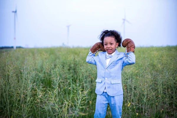 black boy in blue suit with boxing gloves standing in a field