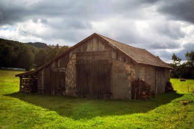 Yeşil bir tarlanın ortasında bir ahır ve bulutlu bir gökyüzü