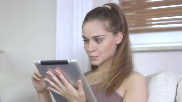 Junge Frau sitzt mit digitalem Tablet auf Couch und studiert — Stockvideo