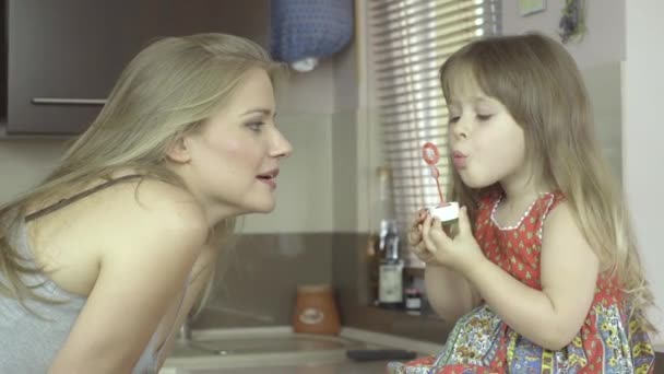 Happy mother and daughter blowing bubbles in the kitchen. — Stock Video