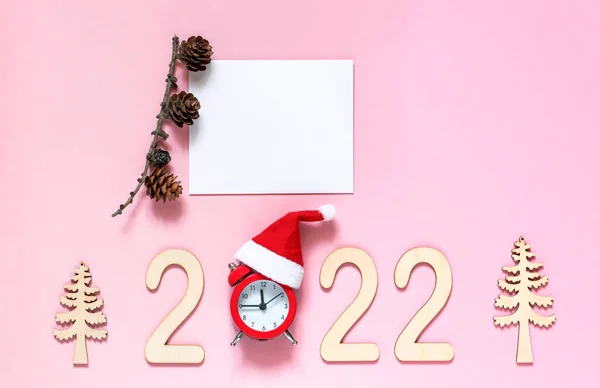 2022 numaralı ahşap arka planda Noel ağacı ve Noel Baba şapkalı bir saat var. Yeni yıl kutlamalarının zamanı geldi. Boş alan, düz uzanma
