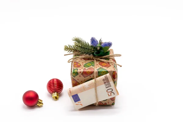 Köknar dalı, 50 Euro 'luk kağıt fatura ve beyaz arka planda Noel ağacı oyuncaklarıyla süslenmiş bir hediye kutusu. Noel tatili için hediye ve sürpriz konsepti