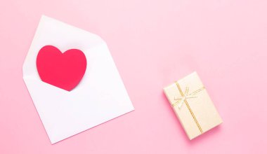 Üzerinde kırmızı kalp olan beyaz bir zarf ve pembe arka planda bir hediye kutusu. Kalpli bir aşk mektubu. Sevgililer Günü 'nde, Anneler Günü' nde, Kadınlar Günü 'nde, aşk mektubunda.