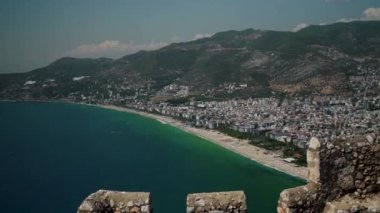 Türkiye - Antalya: Modern şehrin batısındaki Alanya Kalesi 'nden şehir evleri ve dağlara karşı ünlü bir Kleopatra Sahili' ne doğru geniş açılı zum. Yukarıdan deniz panoramik görünümü.