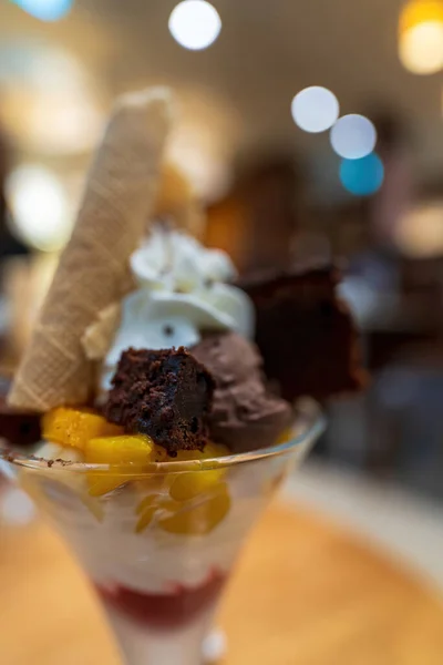 Vanilla and chocolate ice cream with mousse with peaches, bananas, Egg Roll Crispy Biscuit Roll, brownie and whipped cream, against blurred background. Delicious dessert ice cream cup